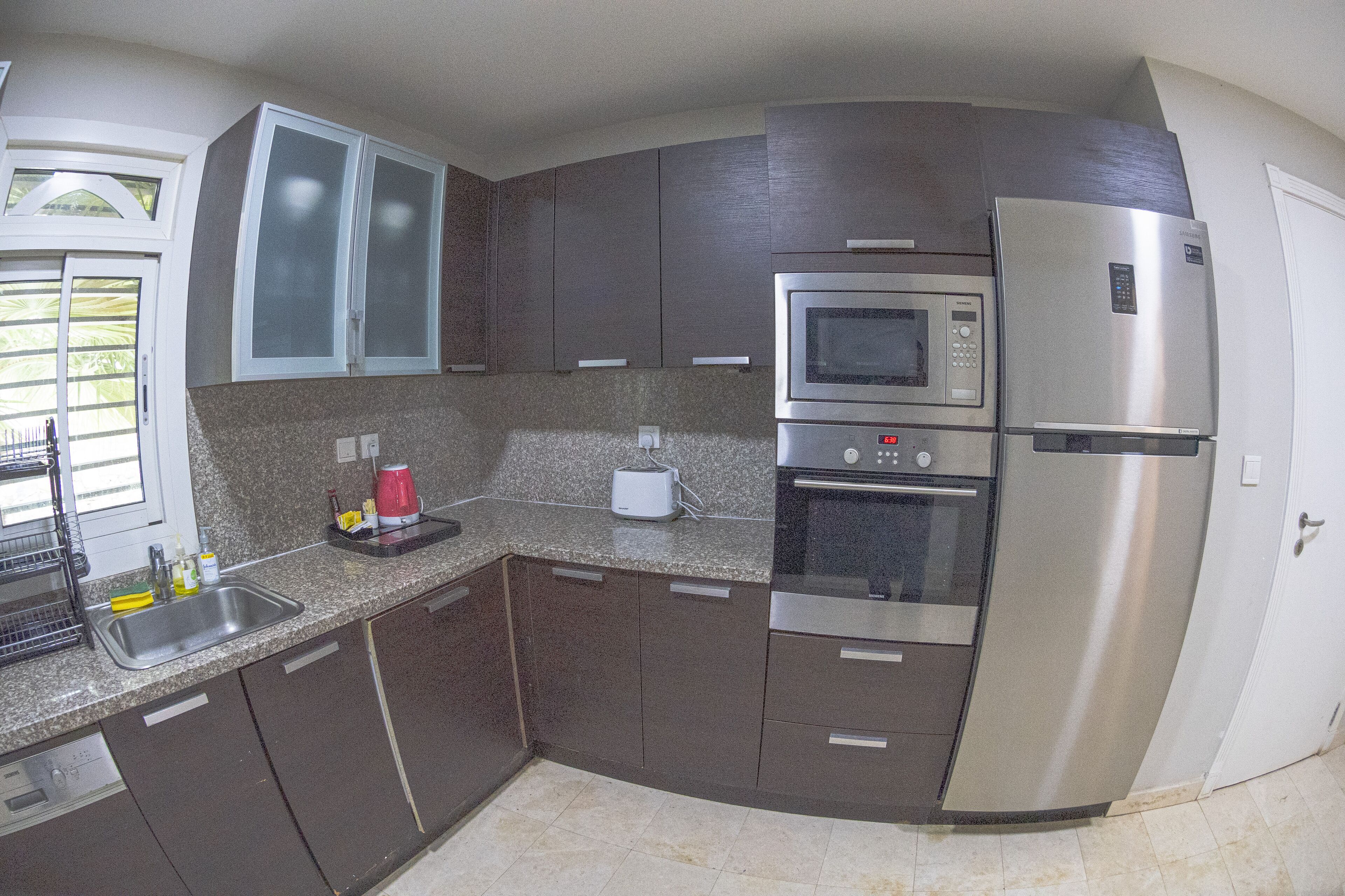 A kitchen with dark cabinets, a stainless steel refrigerator, a microwave, and an oven.