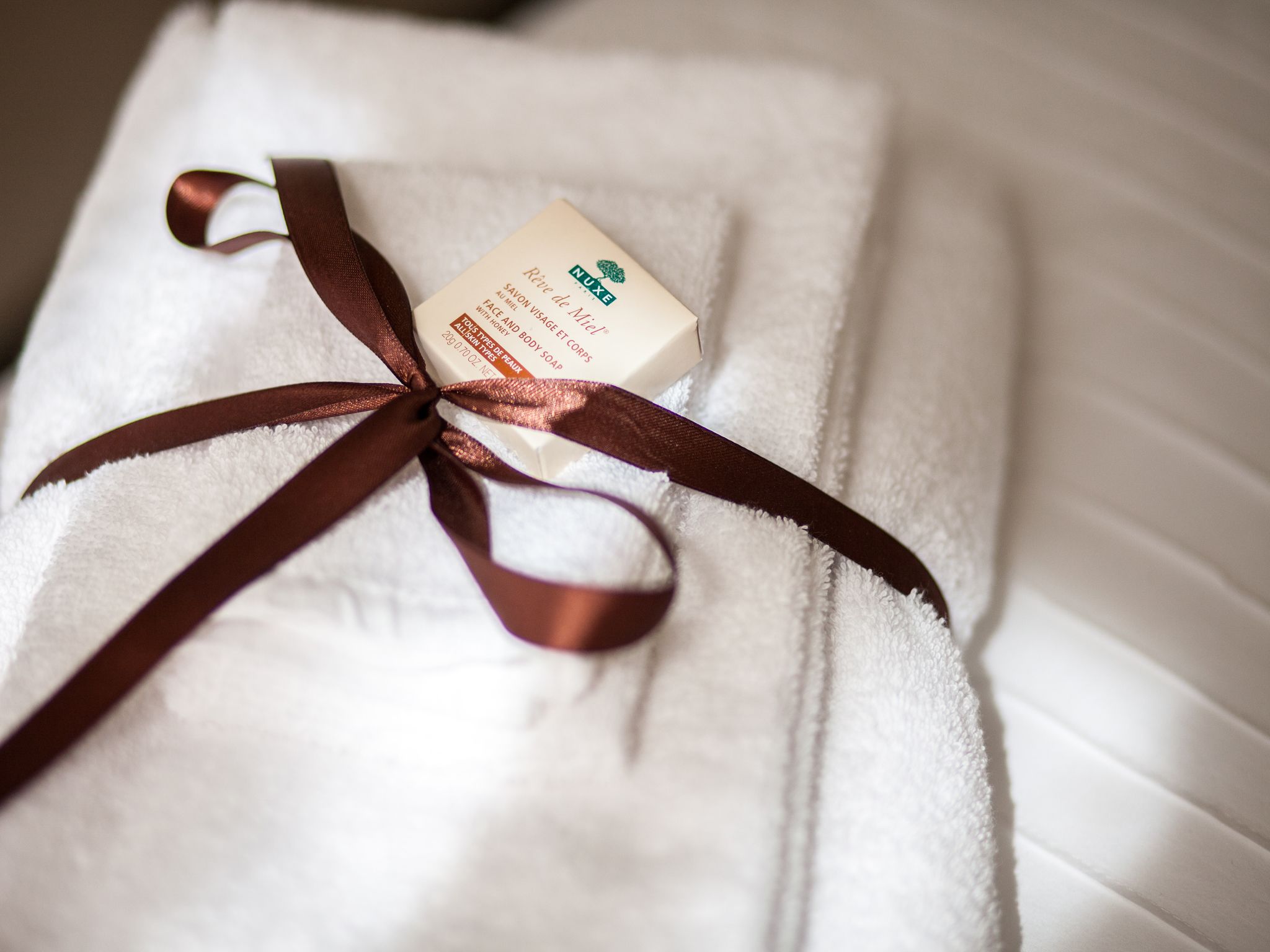 A white towel with a brown ribbon tied around it, placed on a bed.