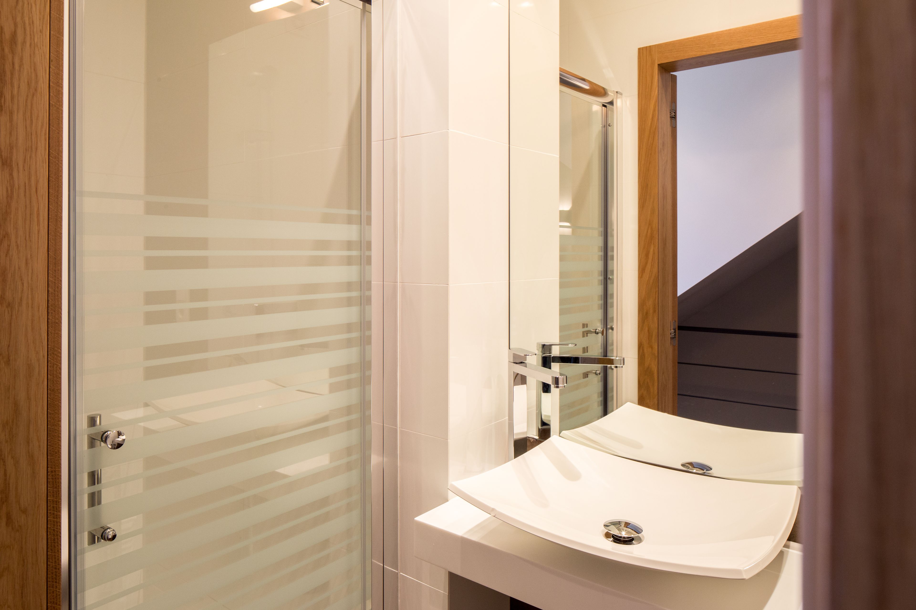 Un bagno moderno con box doccia in vetro, un lavandino bianco con specchio e una finestra con cornice in legno.