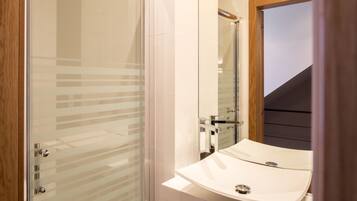 Un bagno moderno con box doccia in vetro, un lavandino bianco con specchio e una finestra con cornice in legno.