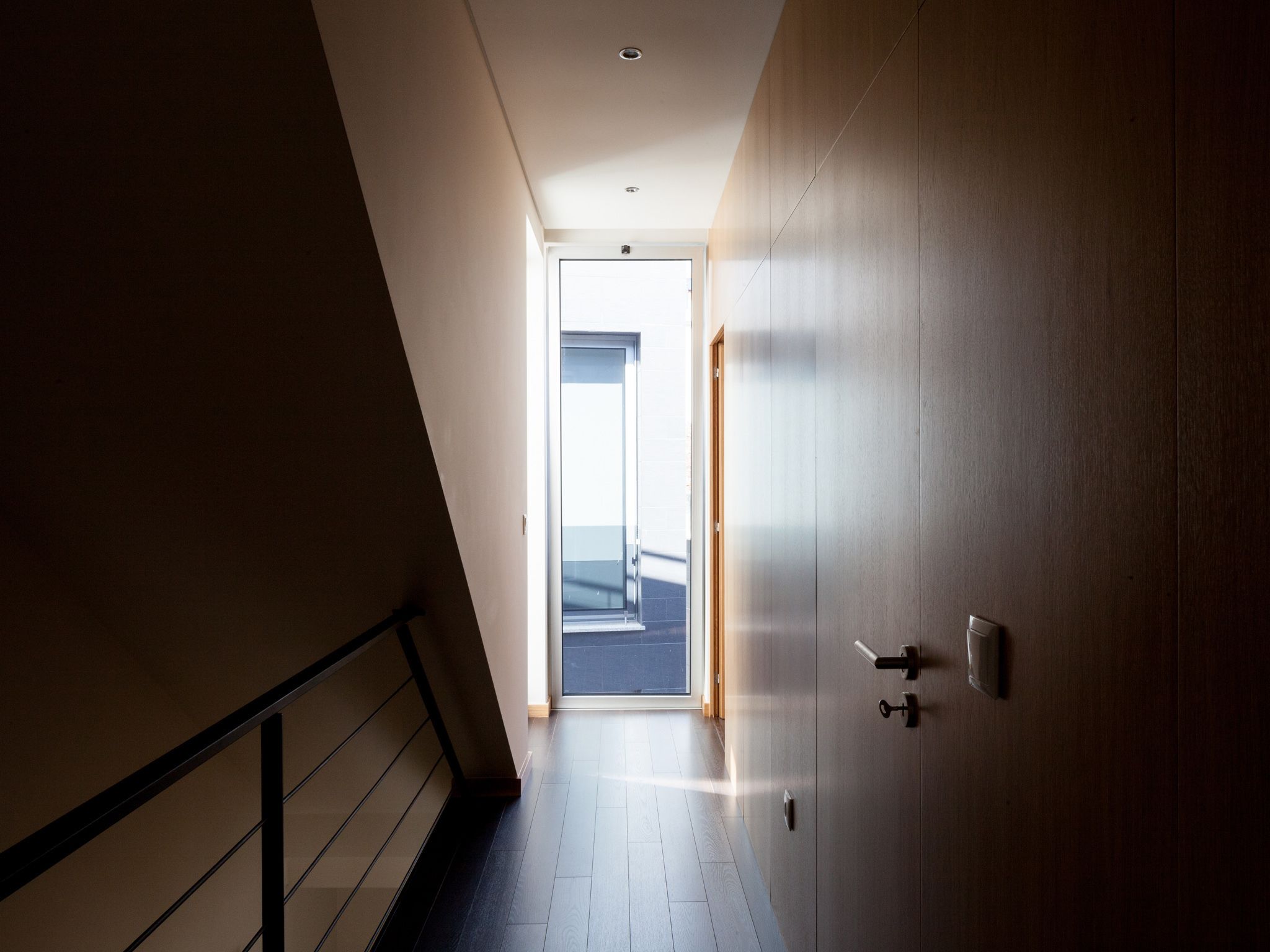 Un corridoio con una porta in legno, una scala e vista su un balcone.