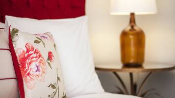 Ein Bett mit weißer Bettwäsche, einem floralen Kissen, einem roten Kopfteil und einer Lampe auf einem kleinen Nachttisch.