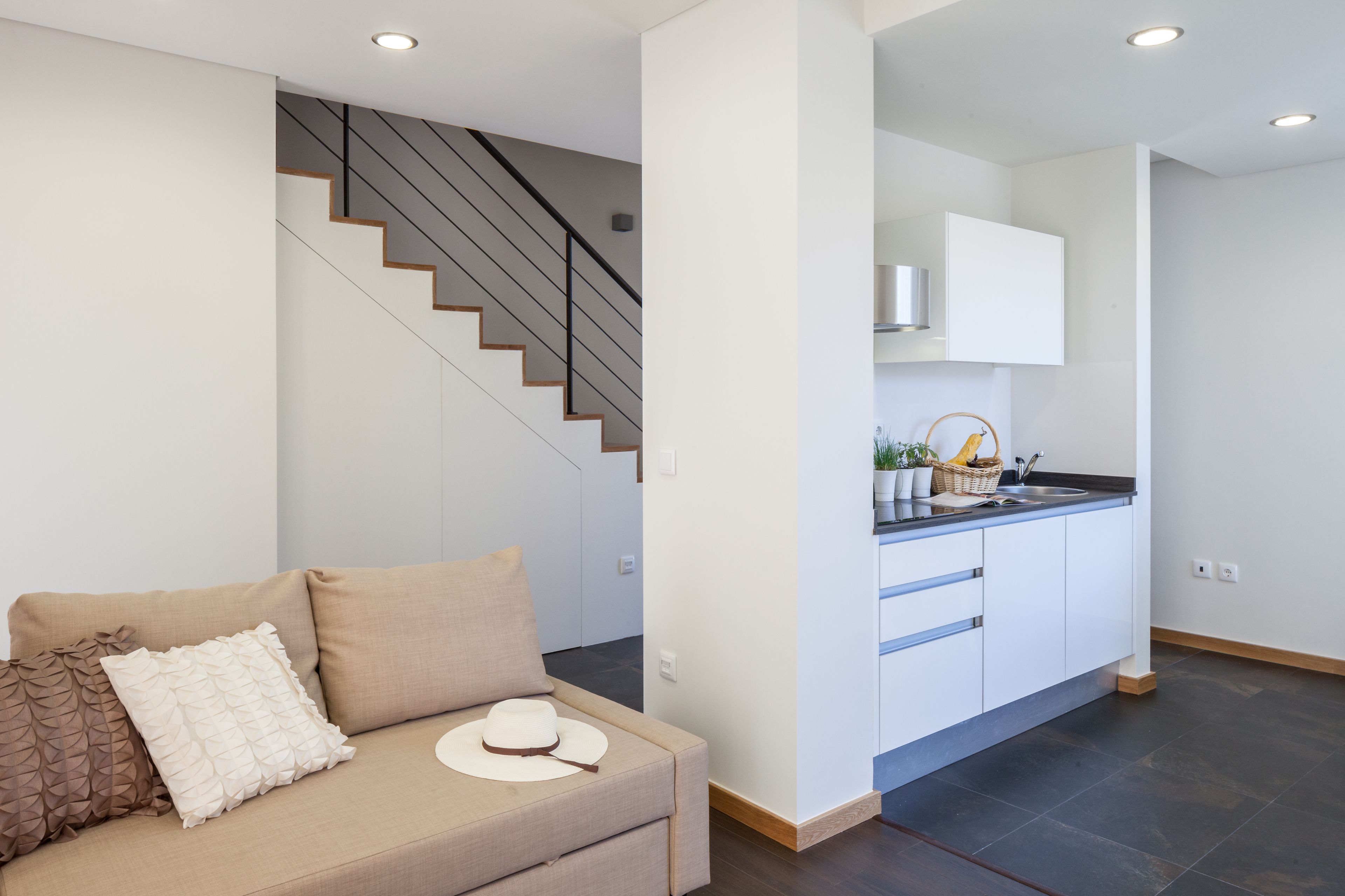 A modern living room with a sofa, a staircase, and a kitchen area.