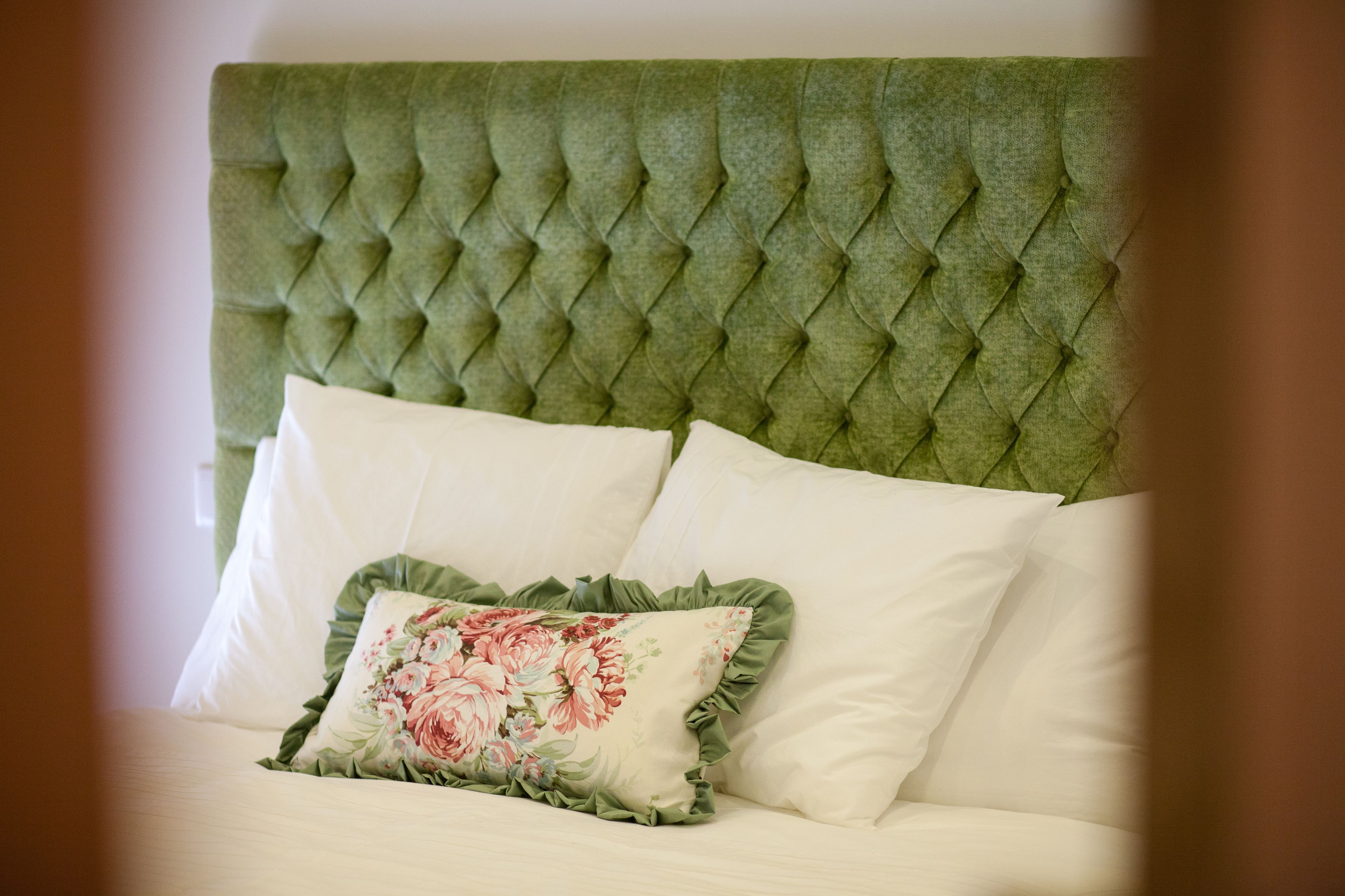 A bed with a tufted headboard, two pillows, and a floral pillow.