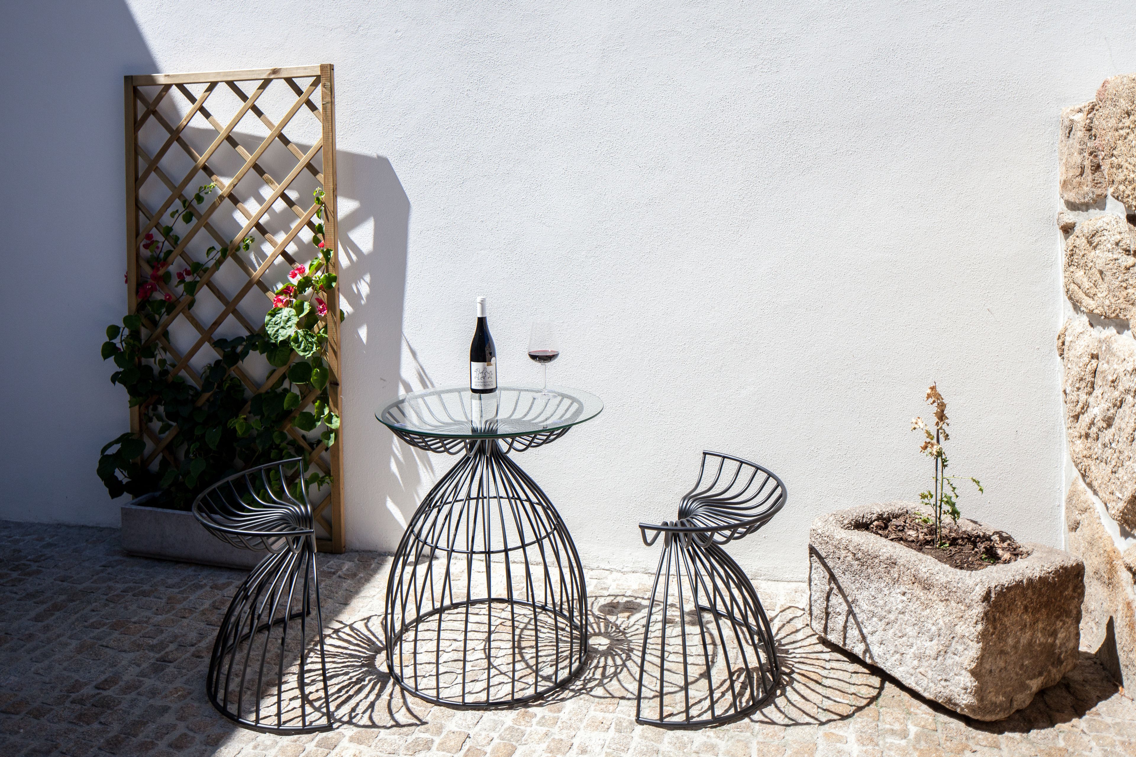 Une terrasse avec une table et des chaises en métal, une plante en pot et une bouteille de vin.