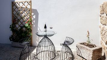 Une terrasse avec une table et des chaises en métal, une plante en pot et une bouteille de vin.