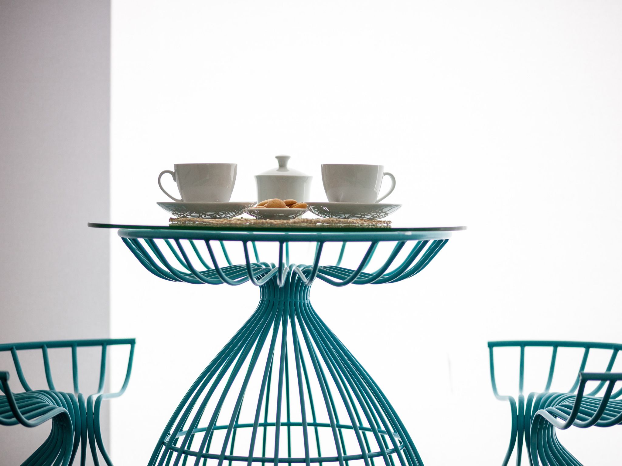 Une table sur laquelle se trouve un plateau avec deux tasses et une théière, le tout posé sur une table en fil de fer assortie à une chaise.