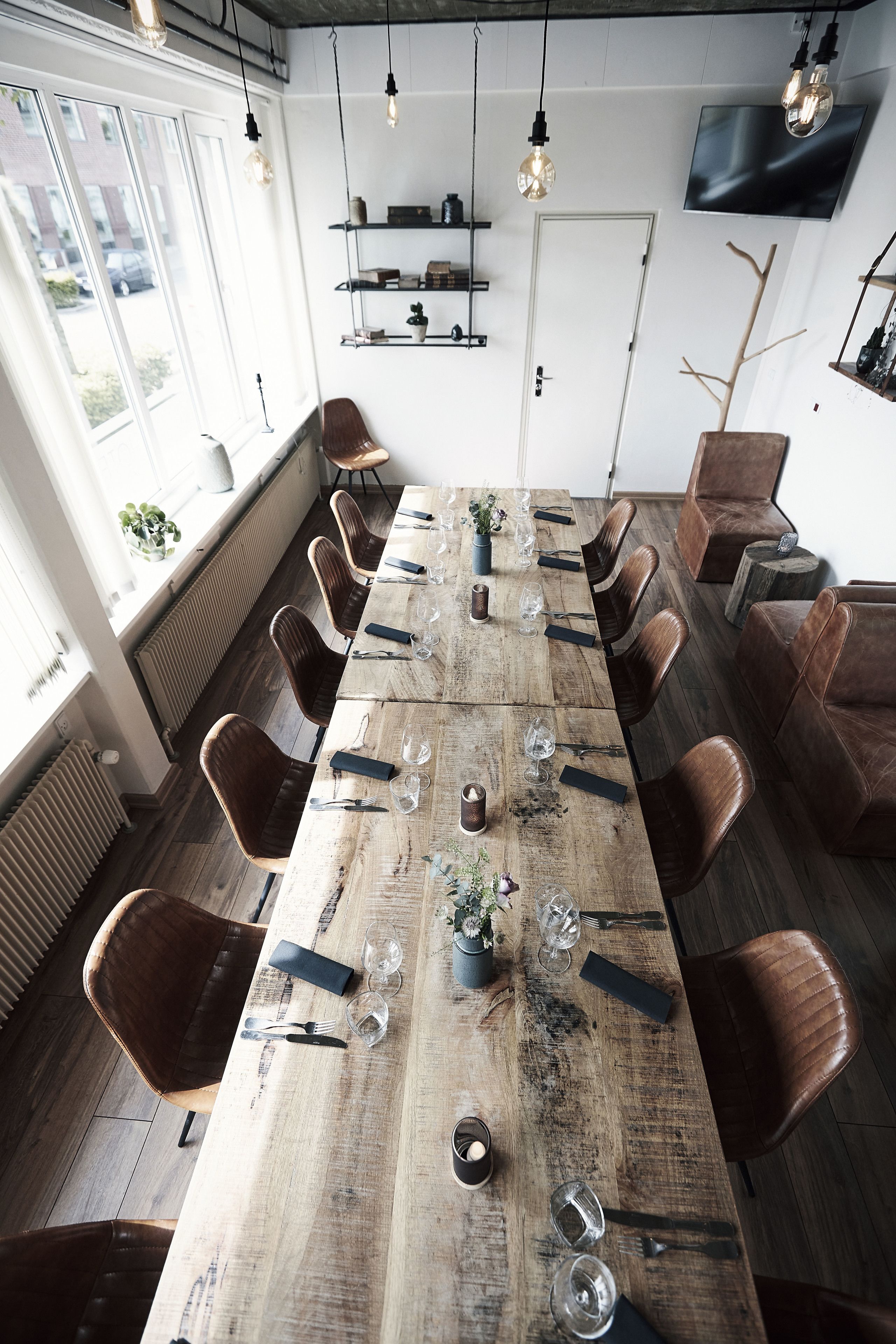 A long wooden dining table set with chairs, surrounded by shelves and a television.