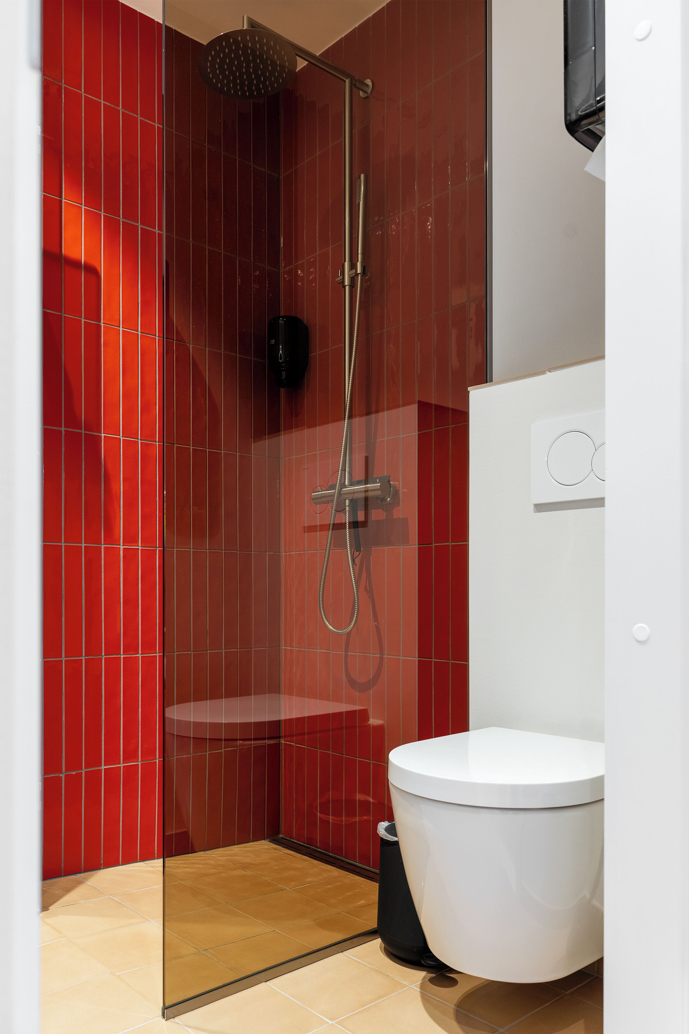 A modern bathroom with a glass-enclosed shower, a white toilet, and red tiled walls.