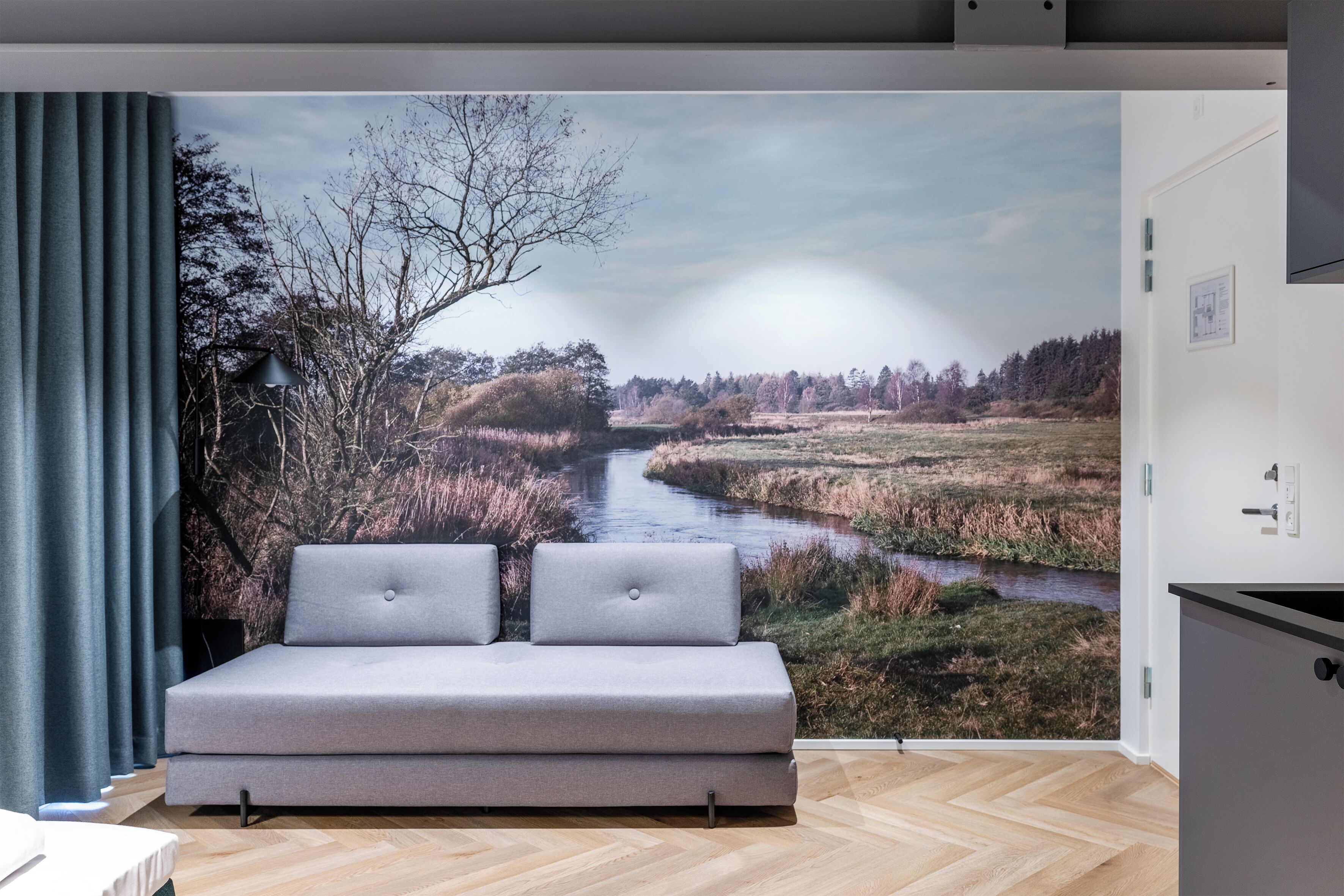 A bedroom with a large window, a grey sofa, and a view of a river landscape.