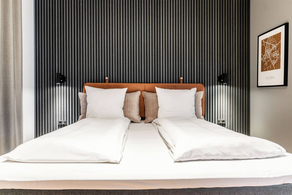 Una cama doble con ropa de cama blanca, un cabecero de madera y dos lámparas de noche.