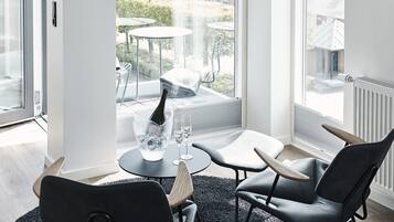 Et moderne værelse med et cirkulært tæppe, to sorte stole, et lille bord og en champagneflaske. Store vinduer giver udsigt til omgivelserne.