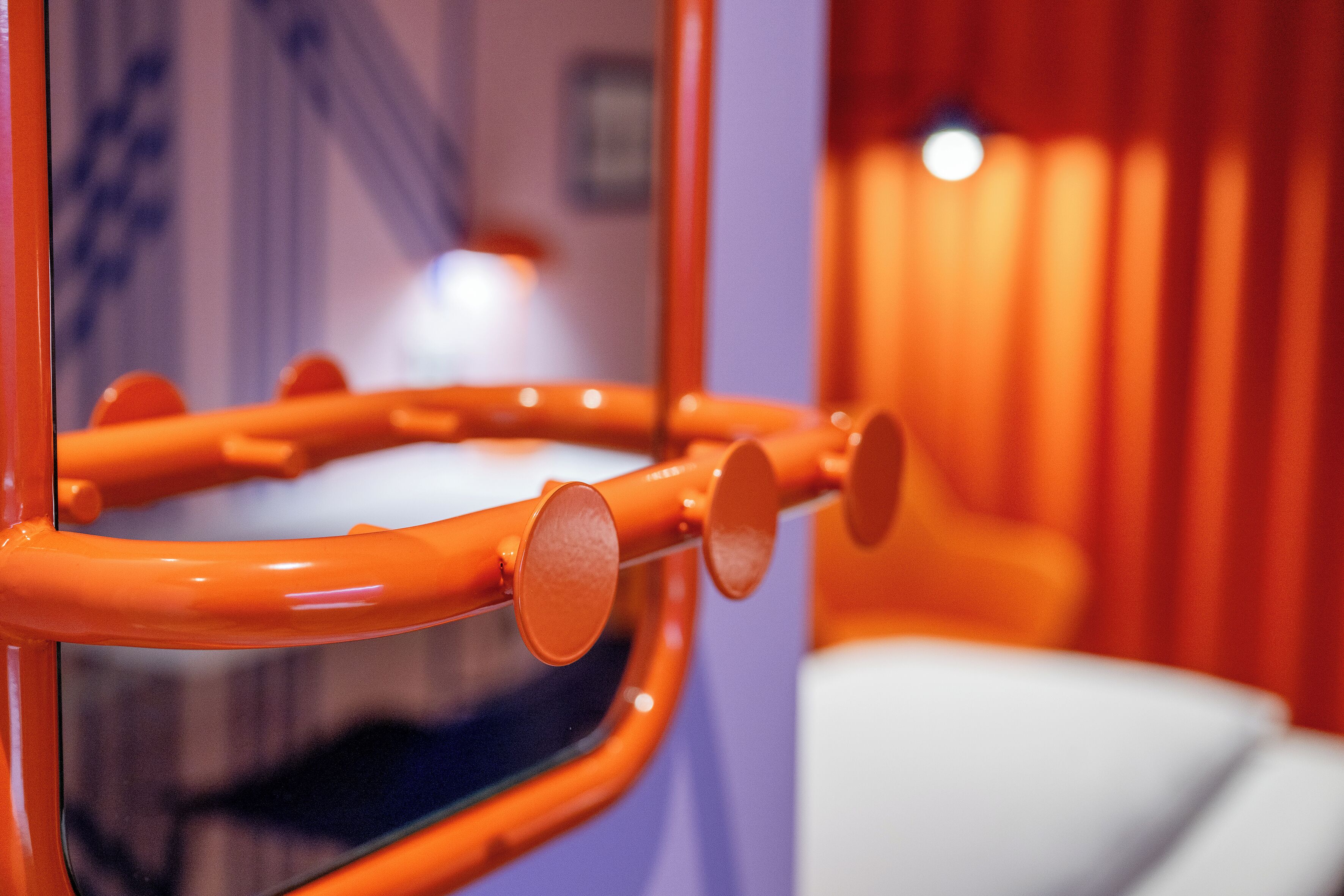 Detailaufnahme einer gewölbten, orangefarbenen Metallstruktur mit runden Elementen, vermutlich ein Teil der Innenraumgestaltung eines Raumes.