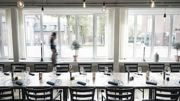 A dining area with multiple tables set for service, large windows with a view of the street, and hanging light fixtures.