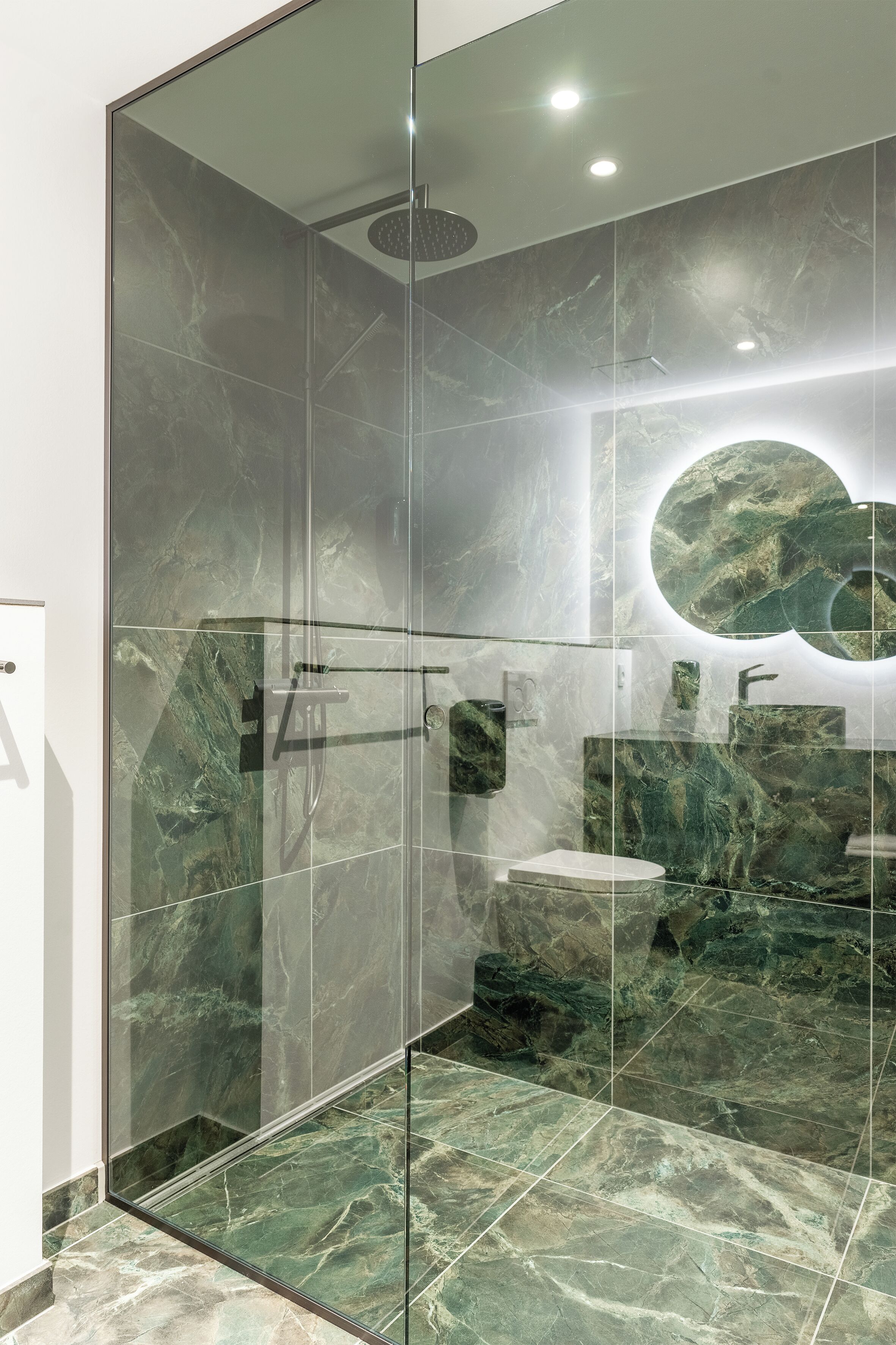 Een moderne badkamer met een douchecabine van glas, marmeren tegels en een ronde spiegel.