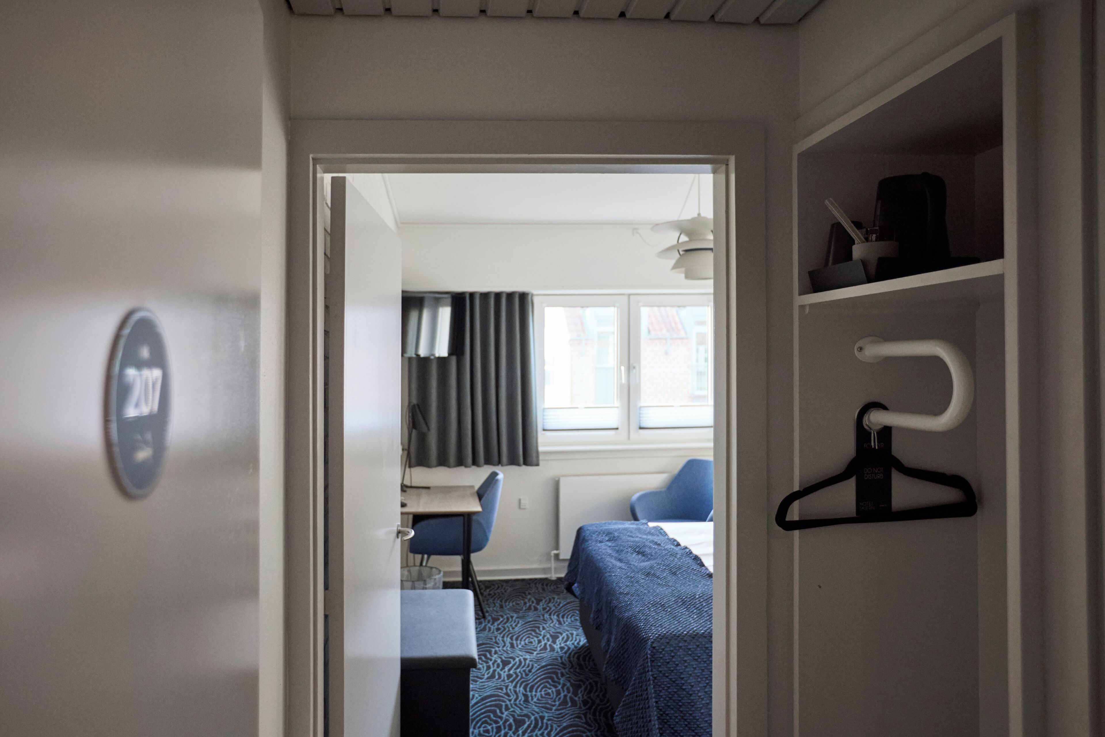 Une chambre d’hôtel avec un lit, un bureau, une chaise et une armoire.