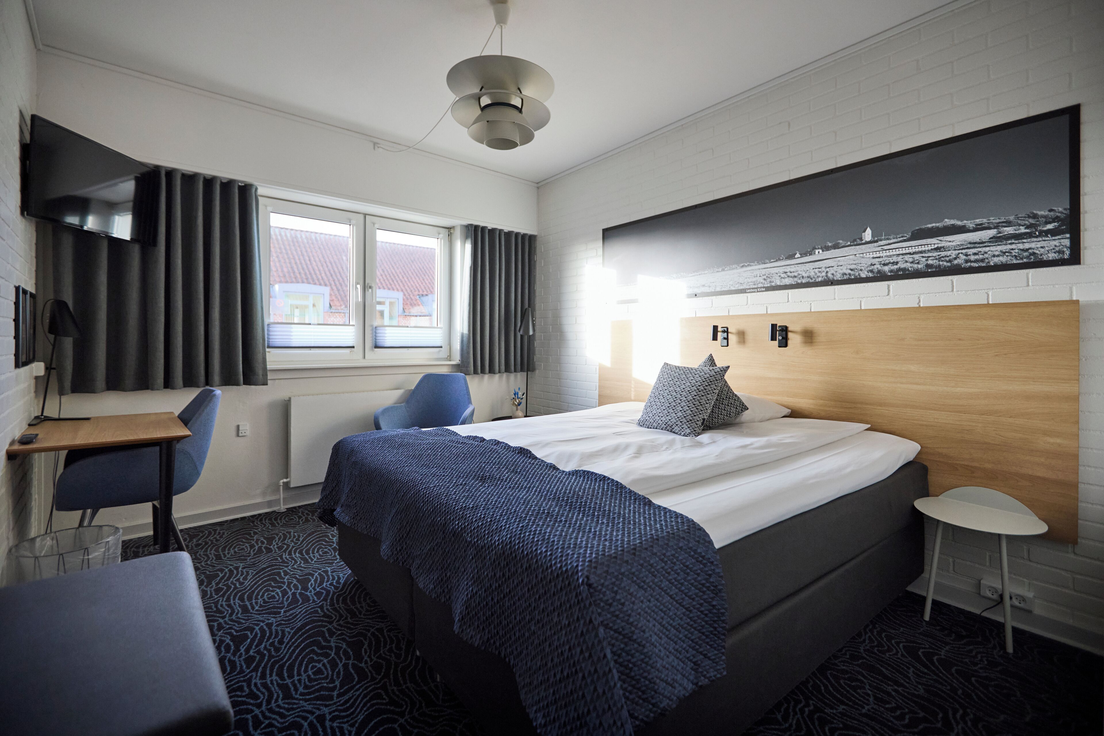 A modern hotel room with a large bed, a desk, a chair, and a view of the outside.