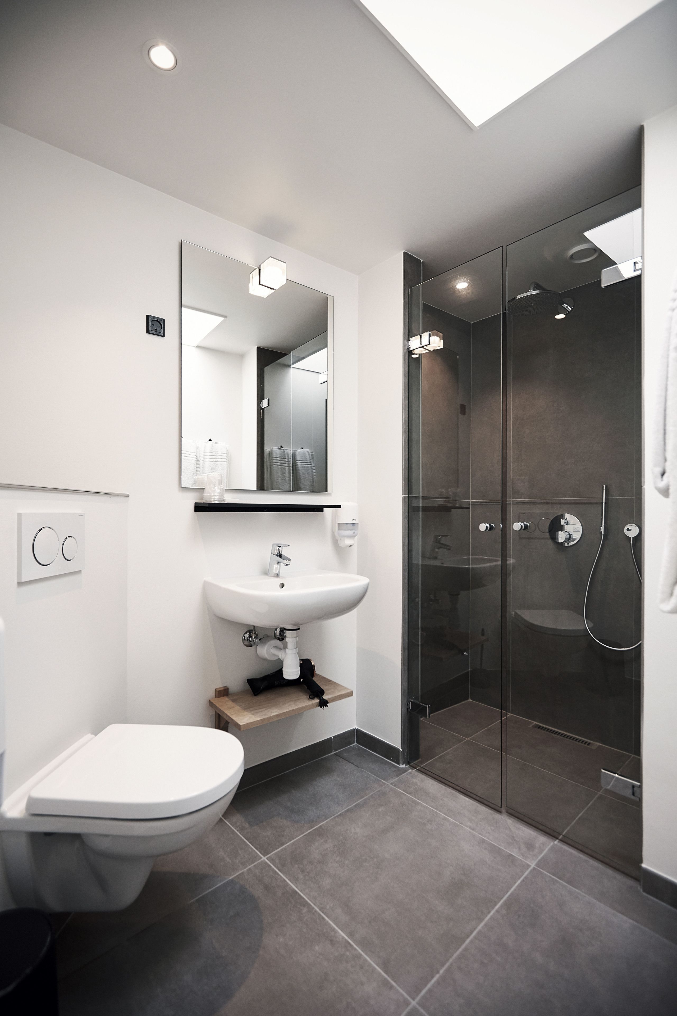 Un baño moderno con inodoro, lavamanos y ducha con mampara de vidrio.