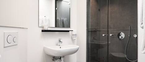 Un baño moderno con inodoro, lavamanos y ducha con mampara de vidrio.
