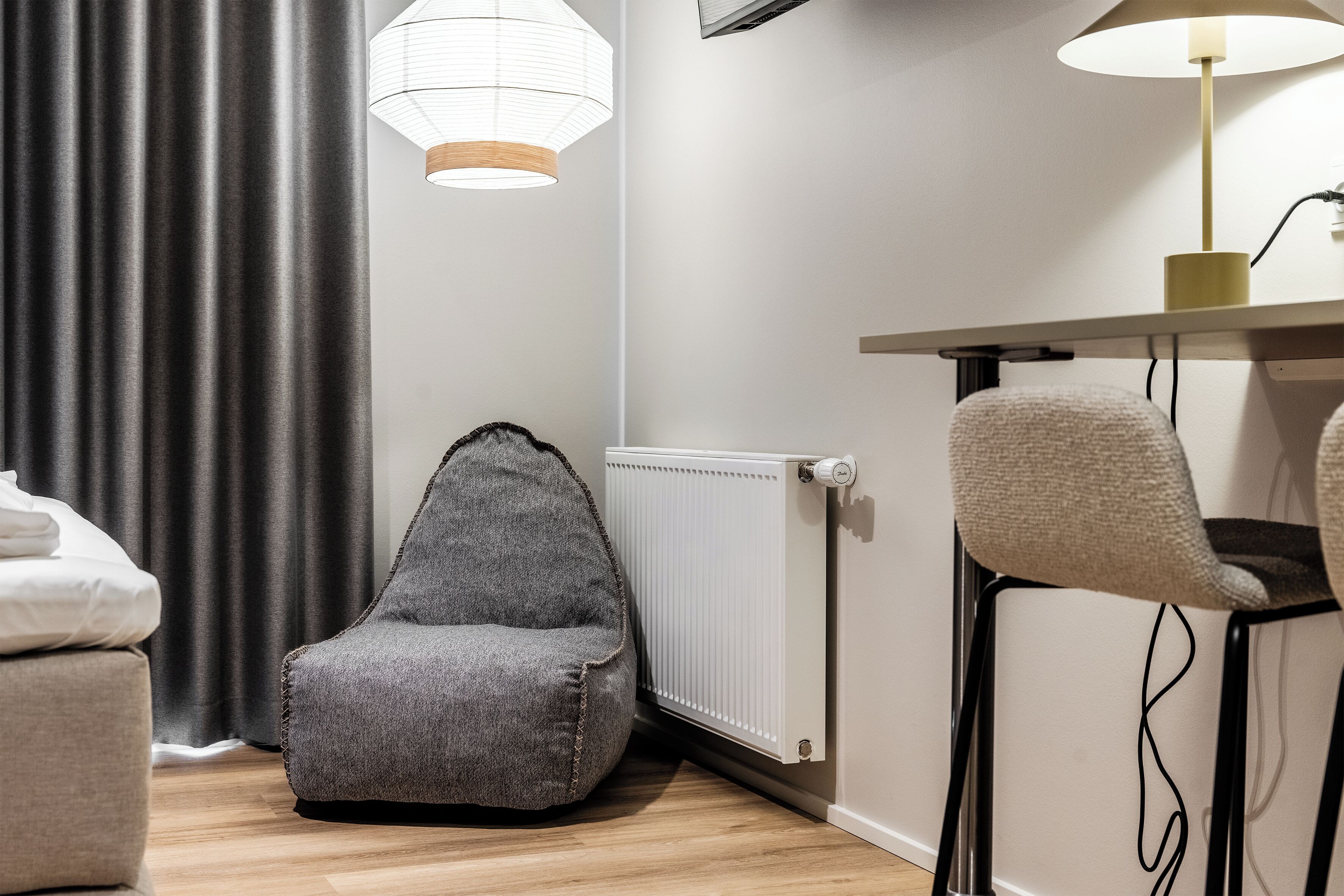 A modern room with a grey bean bag chair, a small table with a lamp, and a radiator.