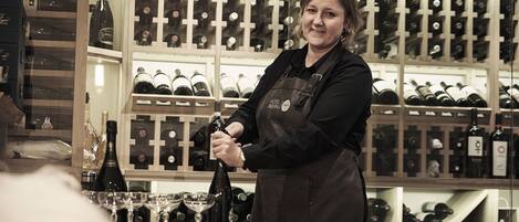 A person in an apron at a bar with a wine rack in the background.