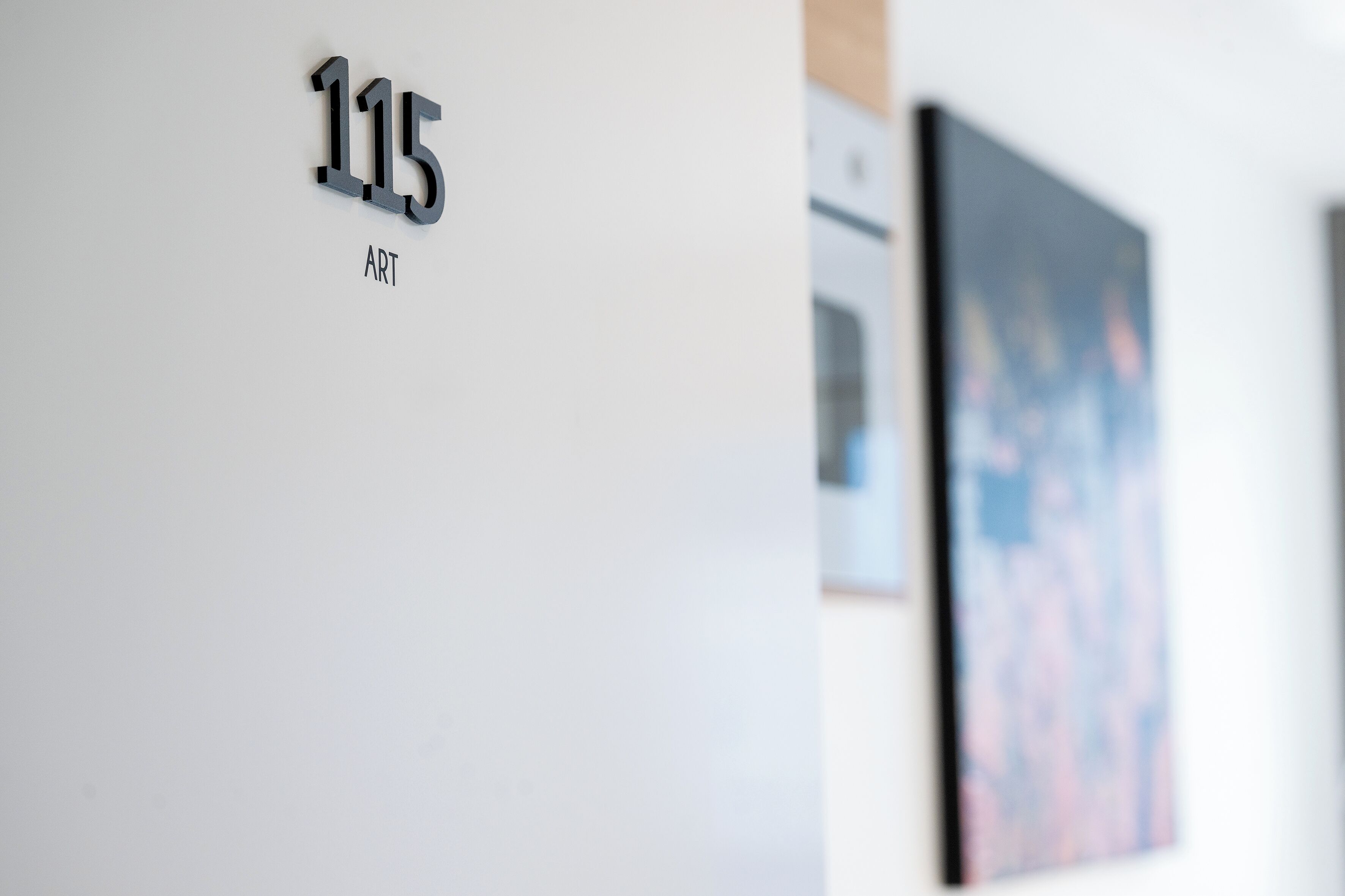 Una pared con el número '115' y la palabra 'ART' debajo, indicando una galería de arte o espacio de exhibición.