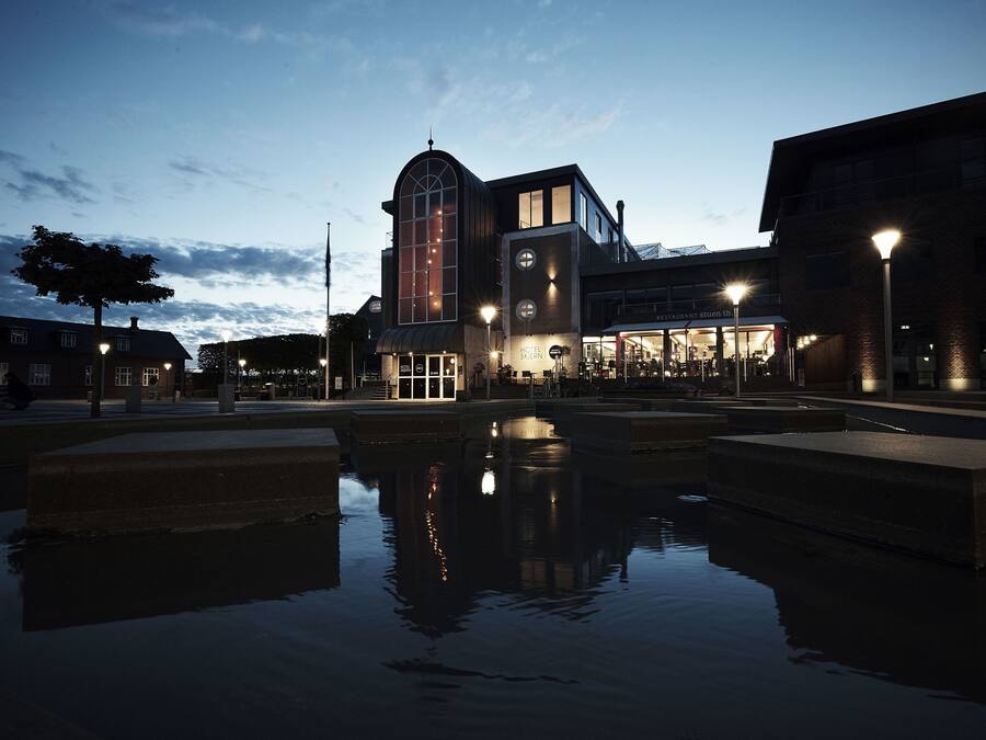 A building with a large arched window and a clock tower, reflecting in a water feature.