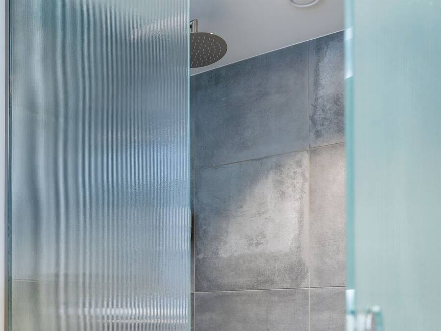 A modern bathroom with a glass shower enclosure, tiled walls, and a visible showerhead.