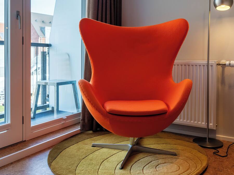 Una habitación moderna con un ventanal grande, un sillón naranja brillante, una lámpara de pie y una mesita.