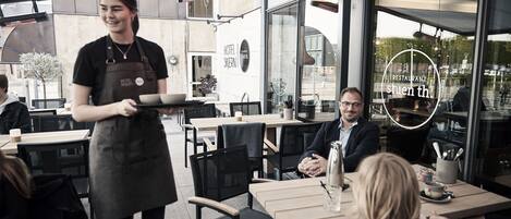 A restaurant with outdoor seating, a waiter serving a customer, and a visible menu.