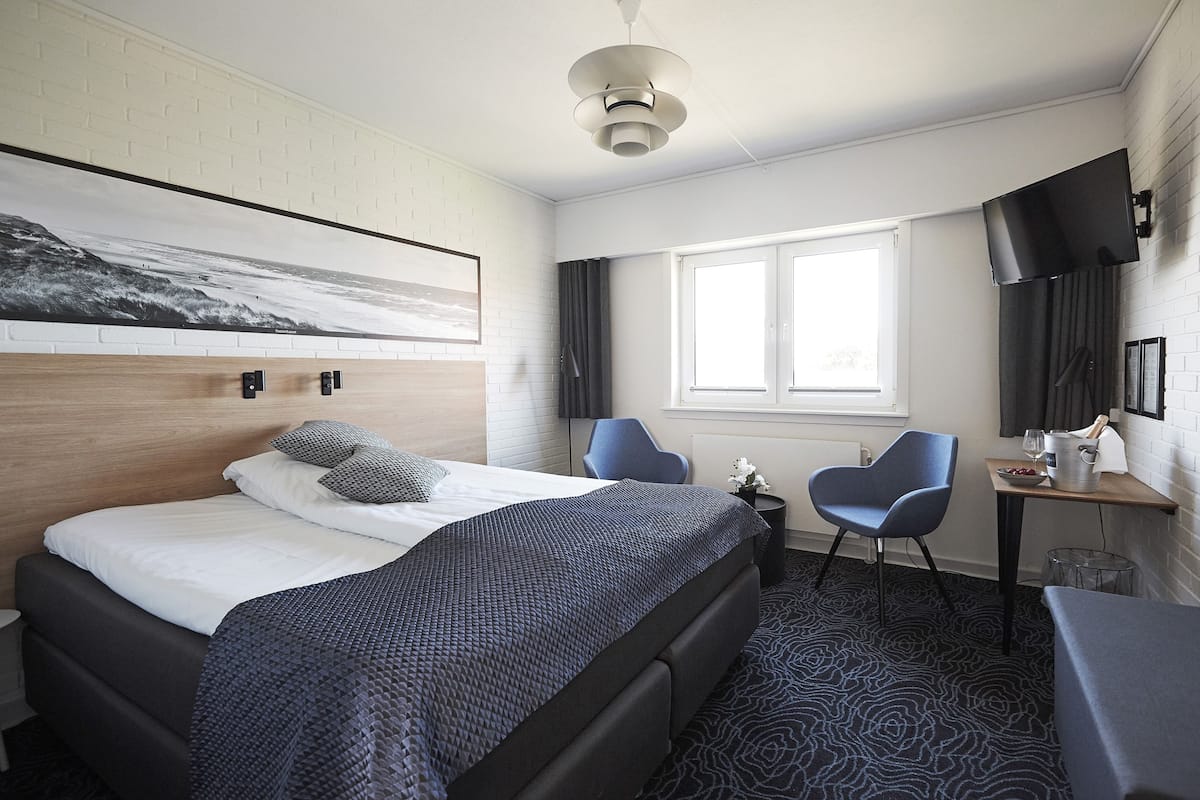 Una habitación de hotel moderna con una cama grande, un escritorio con una silla, un televisor de pantalla plana y una ventana con cortinas.