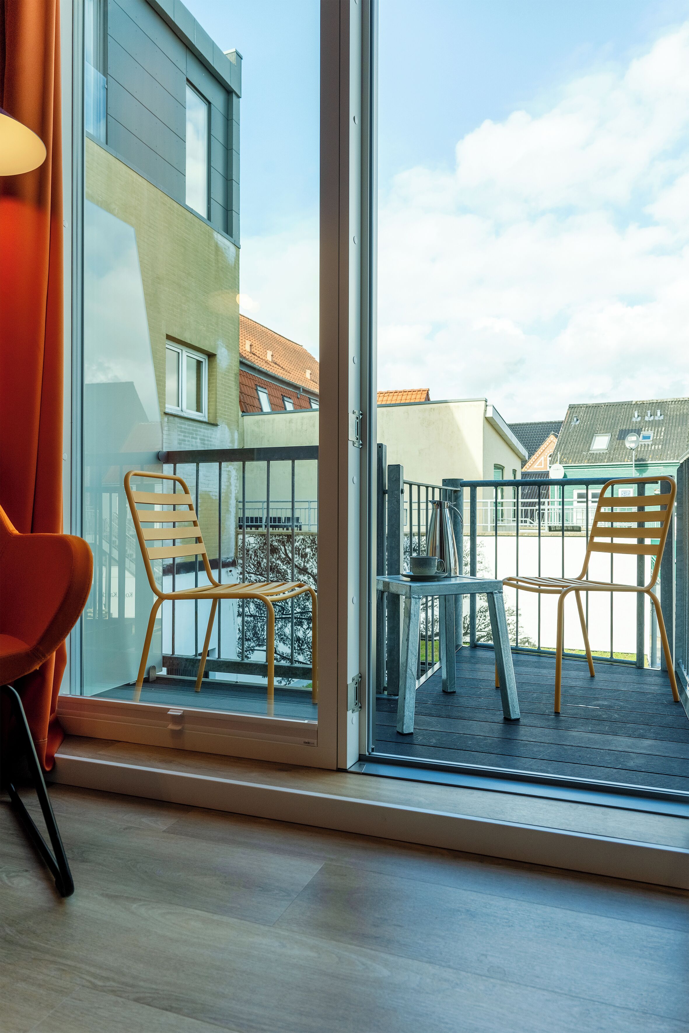 Un apartamento moderno con balcón, dos sillas de madera, una mesa y una silla roja en su interior.