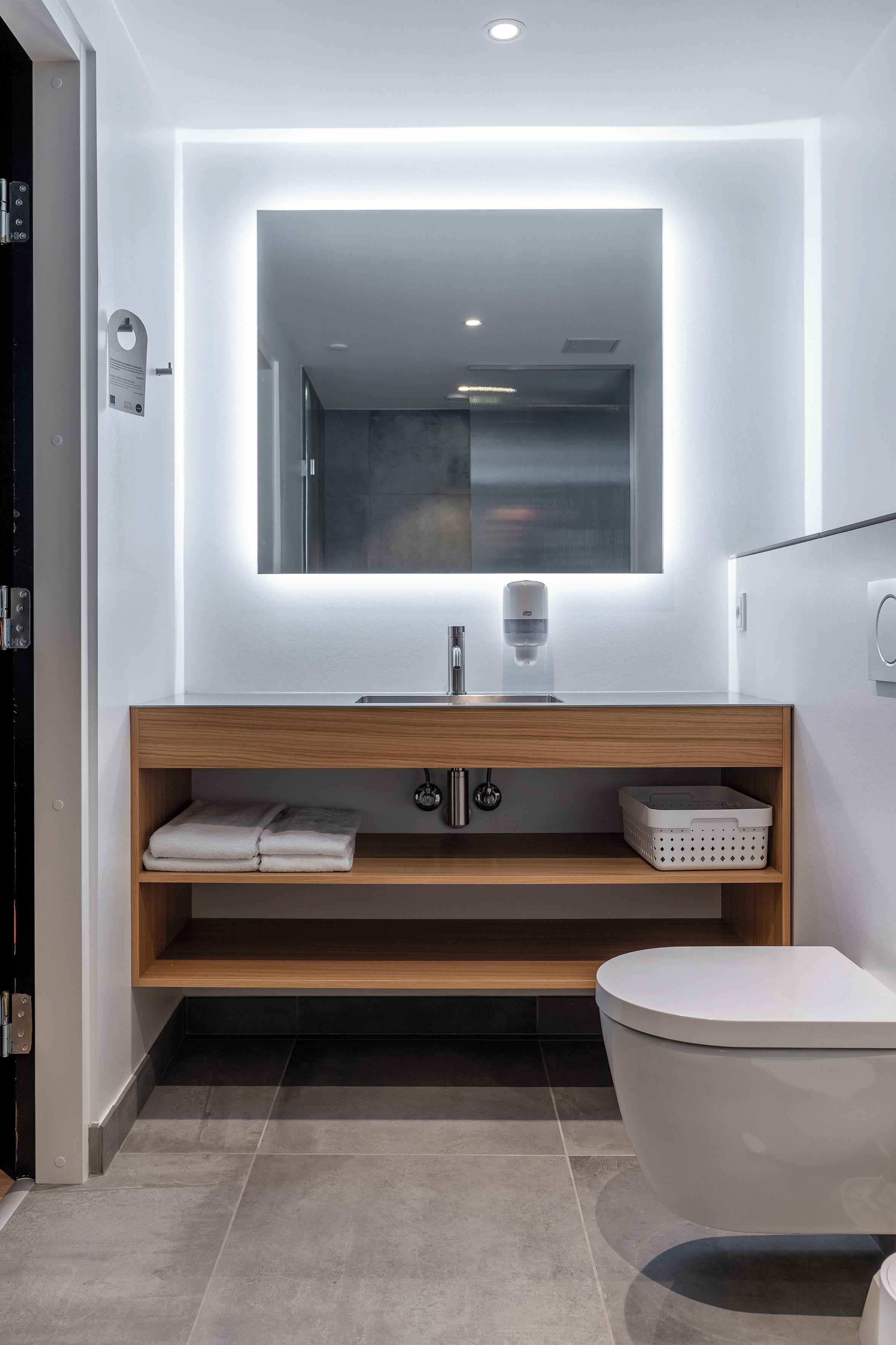 Un baño moderno con tocador de madera, un espejo grande y un inodoro.