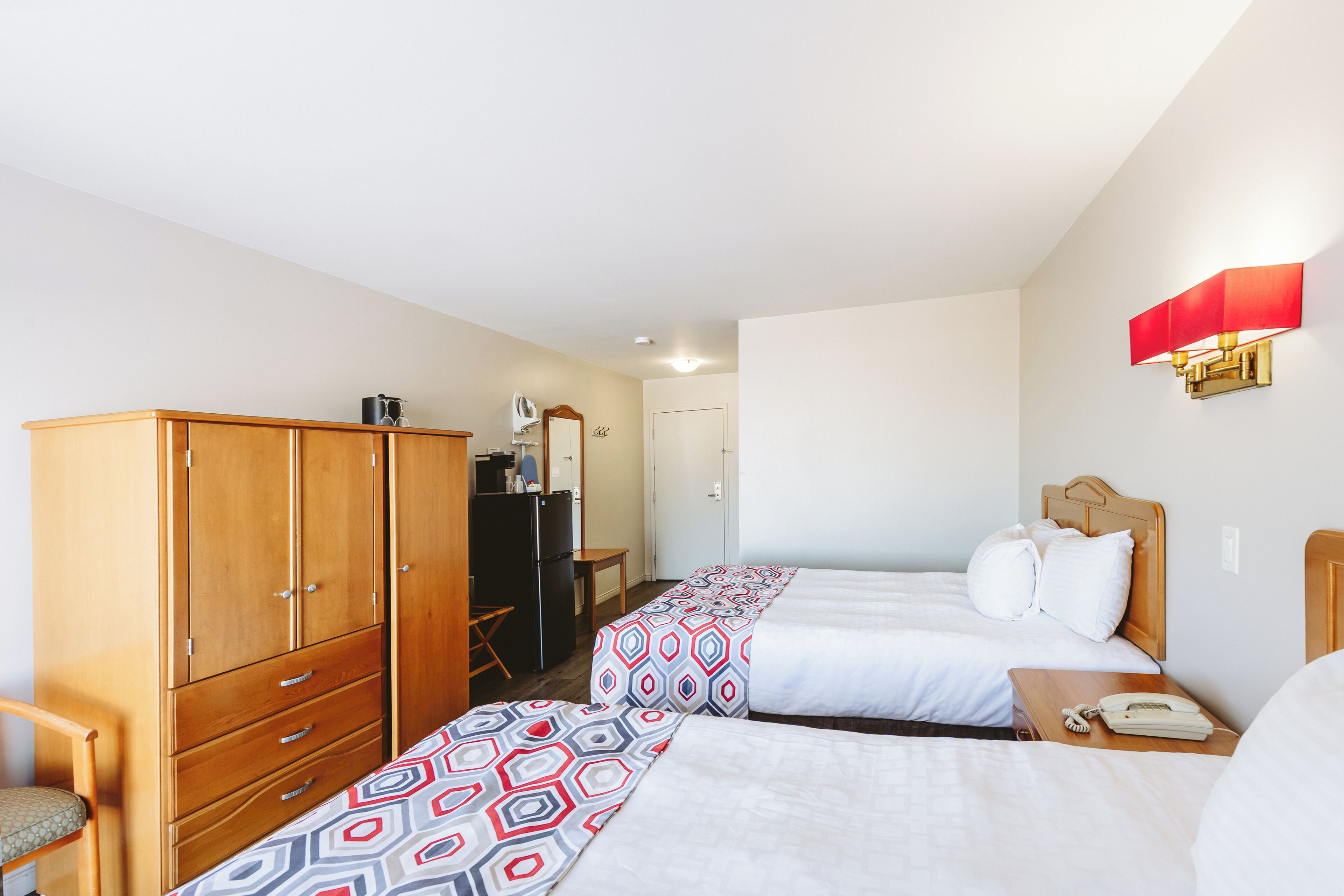 A hotel room with two beds, a wardrobe, a desk, and a mirror.