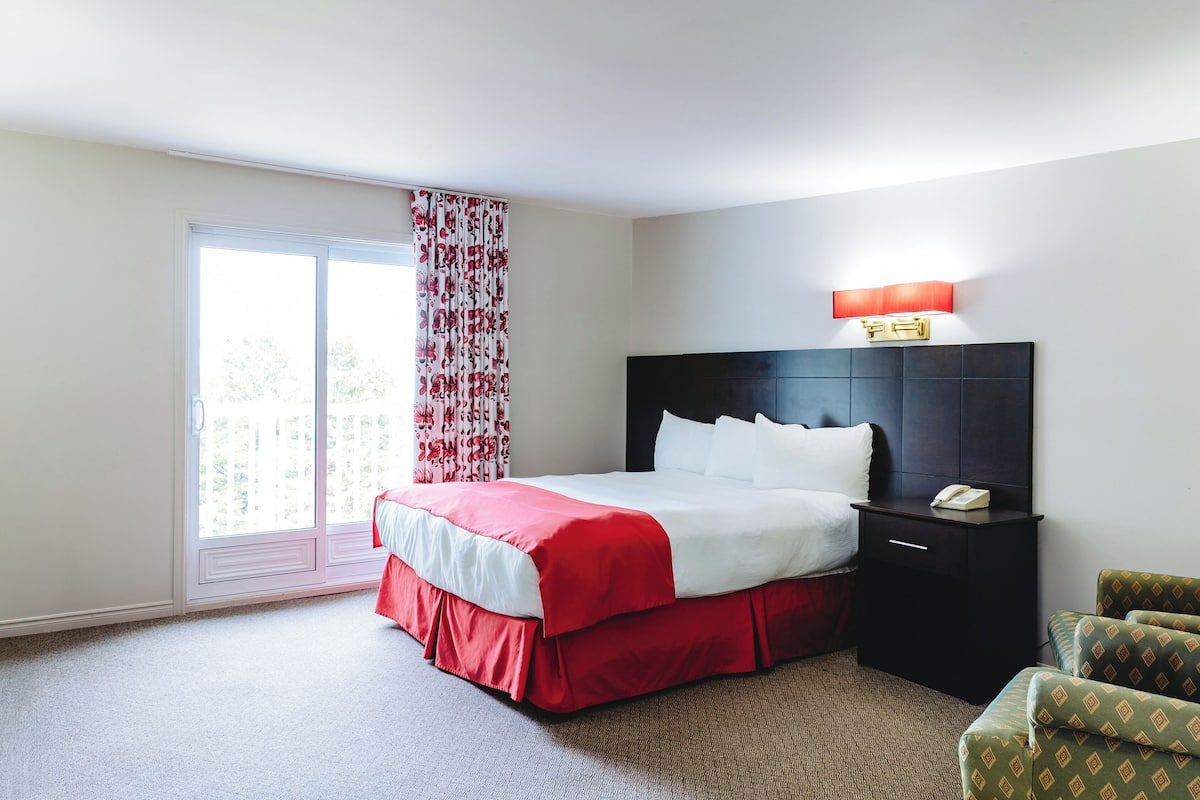 A hotel room with a bed, a nightstand with a phone, a chair, and a window with curtains.
