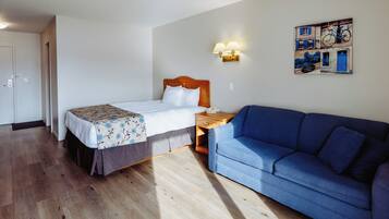 A hotel room with a bed, a blue sofa, a nightstand, a wall-mounted lamp, and a wall art depicting bicycles.