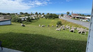 A view of a grassy area with sheep sculptures and a road with buildings in the background. - Mon Joli Motel (Sainte-Flavie)
