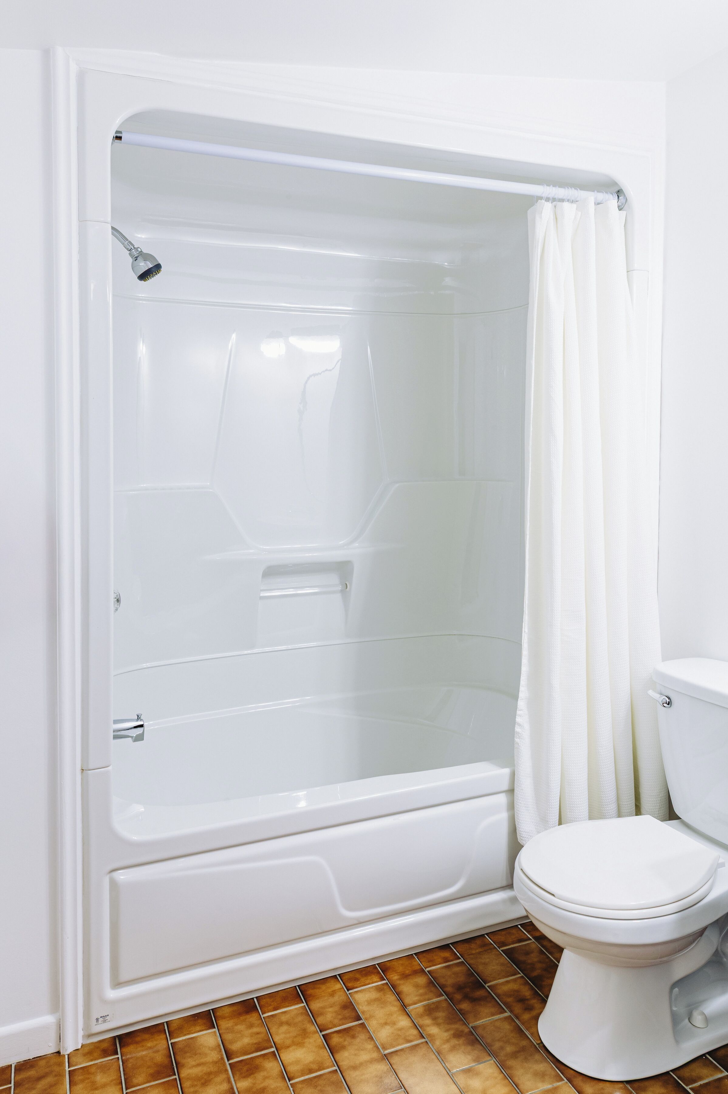 A bathroom with a bathtub, toilet, and brown-tiled floor.