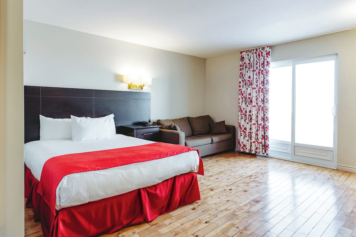 A hotel room with a large bed, a sofa, a small table, and a sliding glass door to the outside.