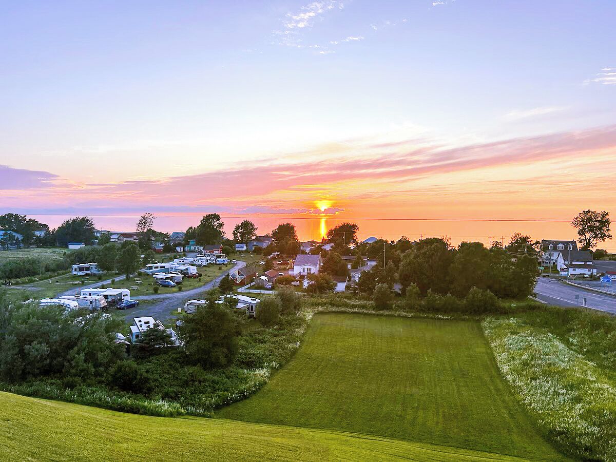 Een camping met campers, een grasveld en huizen op de achtergrond tijdens de zonsondergang.