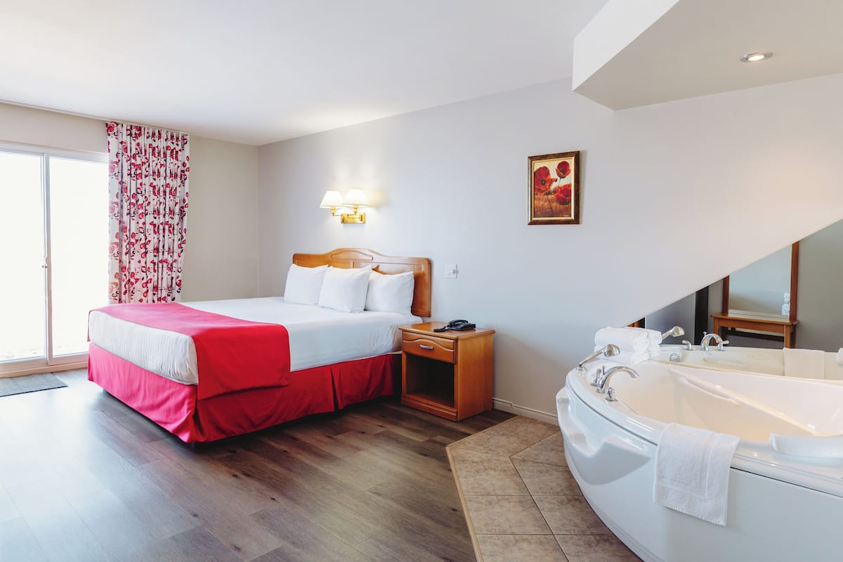 A hotel room with a bed, bedside table, and a large bathtub.
