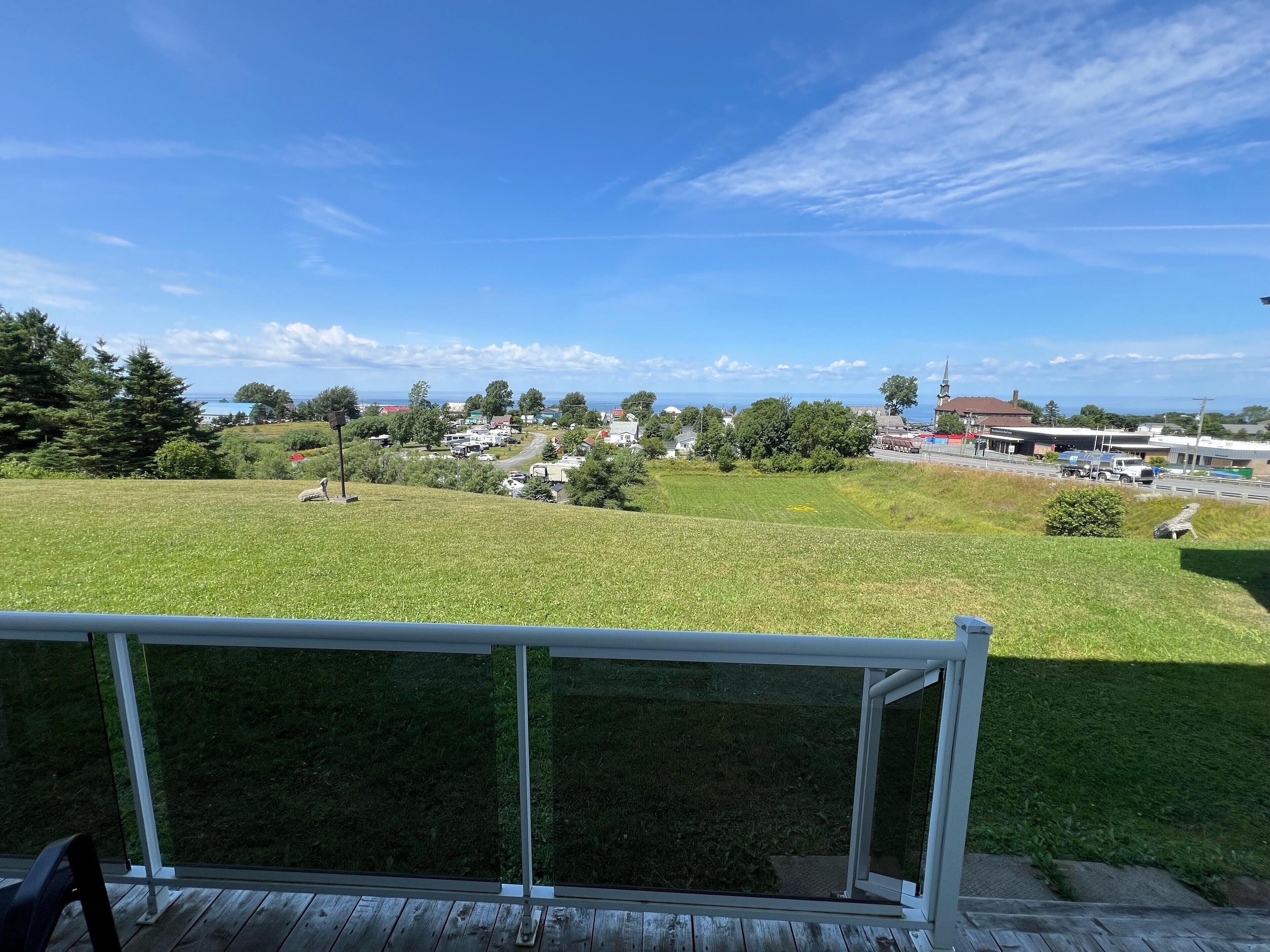 A view from a deck overlooking a grassy area with a distant town and ocean.