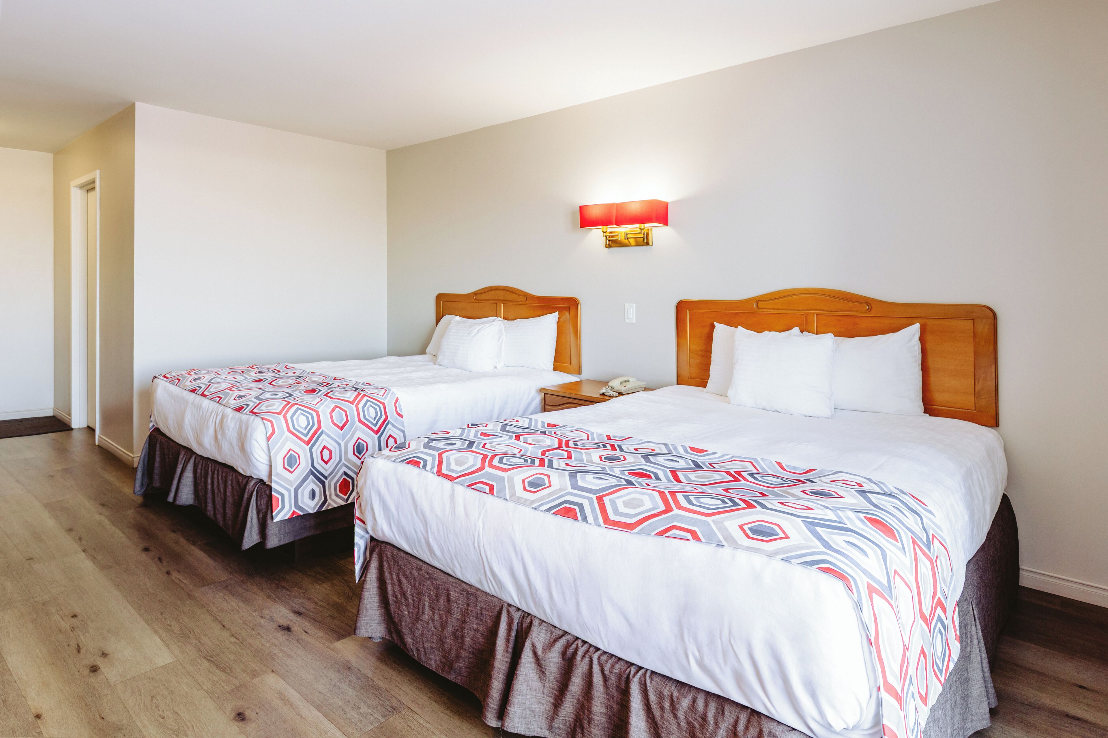 Een hotelkamer met twee bedden, elk met een beddekleed met een patroon en een houten hoofdbord.