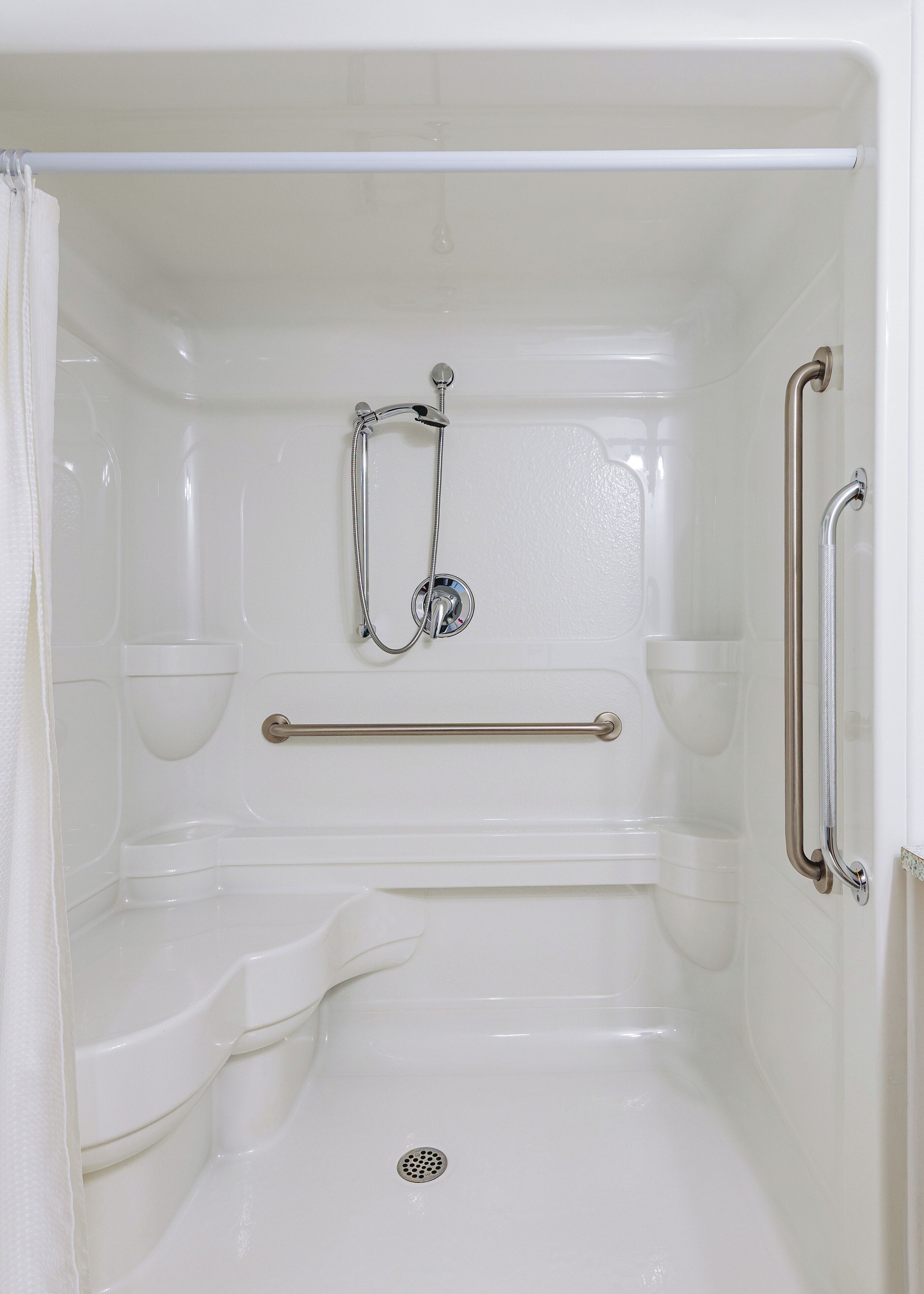 A white, accessible shower stall with a handheld showerhead, grab bars, and a safety grab bar.