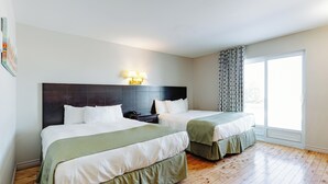 A hotel room with two beds, a dark headboard, bedside lamps, a nightstand, and a large window with curtains. - Mon Joli Motel (Sainte-Flavie)