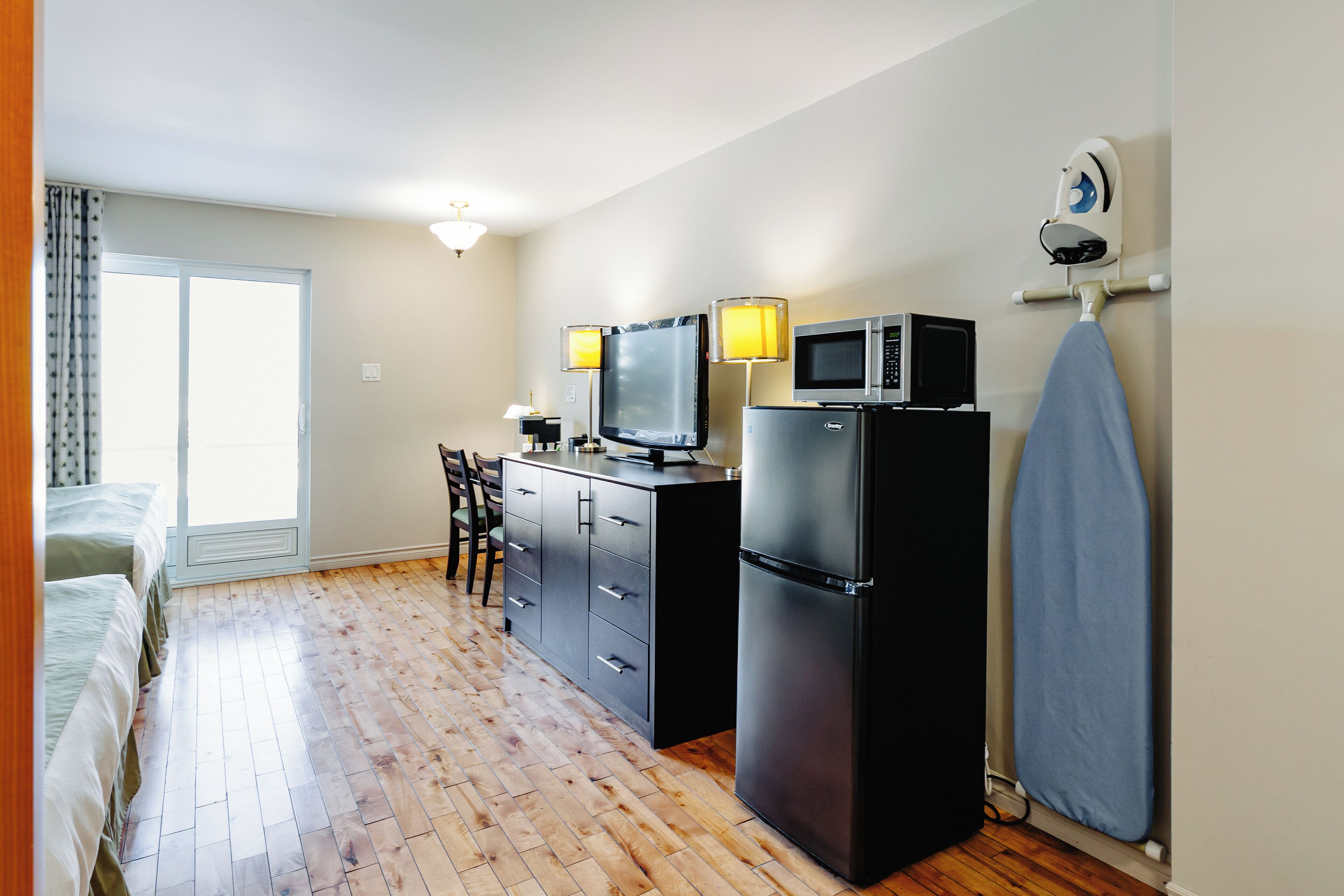 Una habitación compacta con kitchenette, cama, escritorio y un ventanal amplio.