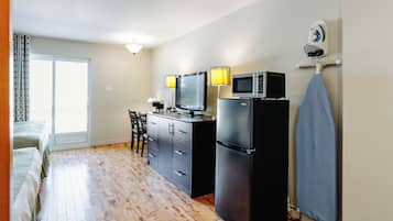 A compact room with a kitchenette, a bed, a desk, and a large window.