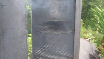 Een verticale grill met eten dat er op bereid wordt, omgeven door groen.