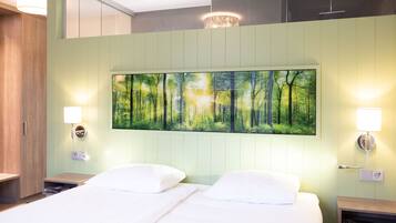 A hotel room with a bed, two bedside tables, a wall-mounted painting of a forest, and a ceiling light fixture.