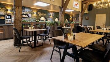 Interno di un ristorante con tavoli e sedie in legno, una zona bar e un'atmosfera rustica.